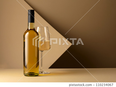 Bottle and glass of white wine on a beige background. Bottle and glass of white wine on a beige background. 110234067