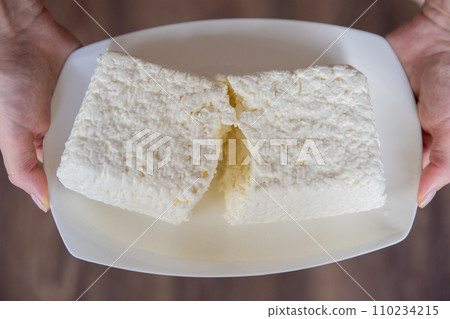 A hand holds a piece of cottage cheese close-up. Eating tasty and healthy foods. A hand holds a piece of cottage cheese close-up. Eating tasty and healthy foods. 110234215