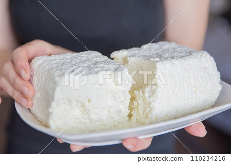 A hand holds a piece of cottage cheese close-up. Eating tasty and healthy foods. 110234216