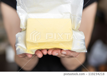 A hand holds butter in a pack close-up. Process of making sandwiches with butter. A hand holds butter in a pack close-up. Process of making sandwiches with butter. 110234218