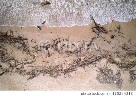An top view of a polluted beach. Ocean waves bring garbage to the shore.The problem of ecology and pollution of nature and the planet. 110234318