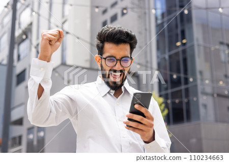 Young successful hispanic man in casual clothes outside office building received online win notification, man celebrating victory triumph, using app on phone, good news in businessman Young successful hispanic man in casual clothes outside office building received online win notification, man celebrating victory triumph, using app on phone, good news in businessman 110234663
