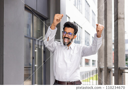 A joyful businessman dances from the outside of the office building, a satisfied man celebrates the victory of Triumph. A joyful businessman dances from the outside of the office building, a satisfied man celebrates the victory of Triumph. 110234670