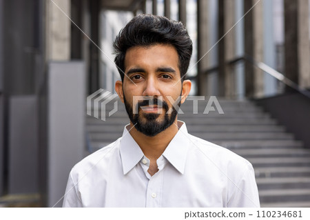 Portrait of a close young businessman, outside the office building, a man is confidently looking in the camera, a worker in the shirt is thinking and focused. Portrait of a close young businessman, outside the office building, a man is confidently looking in the camera, a worker in the shirt is thinking and focused. 110234681
