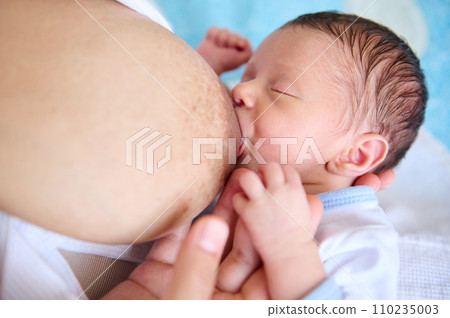 Overhead view adorable newborn baby sucking mother's breast. Close-up conscious loving mother breastfeeding her baby. 110235003