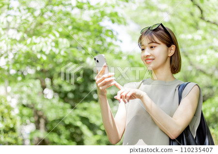 A female college student using a smartphone in the fresh green A female college student using a smartphone in the fresh green 110235407