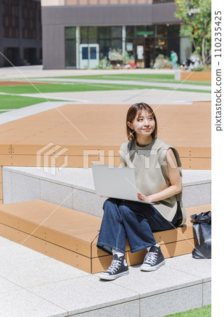 Female college student using a laptop outdoors Female college student using a laptop outdoors 110235425