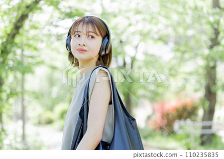 戴著耳機聽音樂的年輕女性,穿著鮮綠色的衣服 戴著耳機聽音樂的年輕女性,穿著鮮綠色的衣服 110235835
