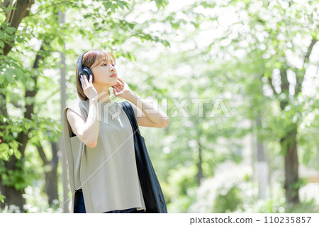 Young woman listening to music with headphones in the fresh green 110235857