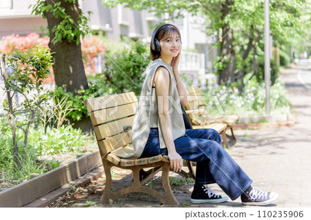 Young woman listening to music with headphones in the fresh green 110235906