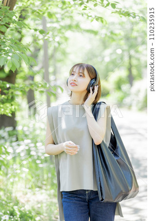 Young woman listening to music with headphones in the fresh green Young woman listening to music with headphones in the fresh green 110235915