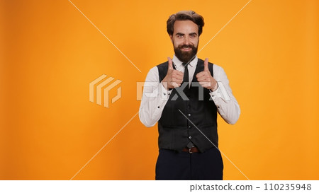 Satisfied waiter does positive gesture while showing his appreciation. Working in the culinary sector, professional staff member gives thumbs up as an excellent statement, like symbol. Satisfied waiter does positive gesture while showing his appreciation. Working in the culinary sector, professional staff member gives thumbs up as an excellent statement, like symbol. 110235948