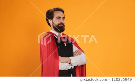 Powerful fantasy hero with red cape standing against yellow background, feeling determined and confident on camera. Dedicated butler acting like superhero, staff member having mantle. Powerful fantasy hero with red cape standing against yellow background, feeling determined and confident on camera. Dedicated butler acting like superhero, staff member having mantle. 110235949