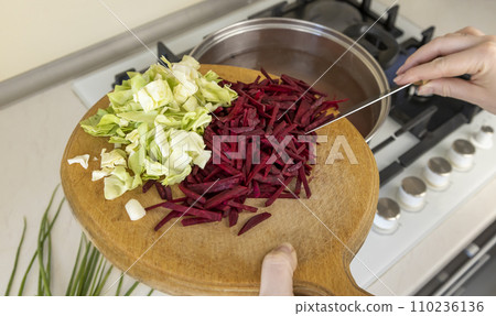 Cabbage and beets are sliced on a wooden board, and the cook adds the cabbage and beets to the cooking broth. Cabbage and beets are sliced on a wooden board, and the cook adds the cabbage and beets to the cooking broth. 110236136
