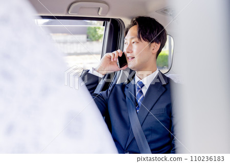 Businessman sitting in the back seat of a taxi talking on a smartphone 110236183