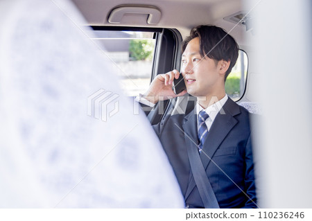 Businessman sitting in the back seat of a taxi talking on a smartphone 110236246