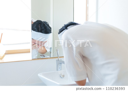 A man washing his face in the bathroom A man washing his face in the bathroom 110236393