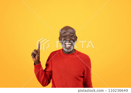 Joyful elderly Black man with white beard laughing and pointing upwards, wearing red sweater 110236649