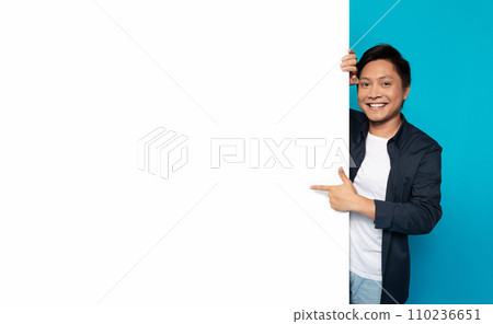 Happy Asian man in casual attire peeking around a large blank white banner Happy Asian man in casual attire peeking around a large blank white banner 110236651