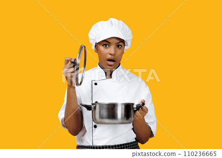 Surprised black female chef lifting lid off pot and looking at camera Surprised black female chef lifting lid off pot and looking at camera 110236665