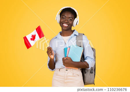 Cheerful millennial black lady student in wireless headphones, with books, flag of Canada 110236676