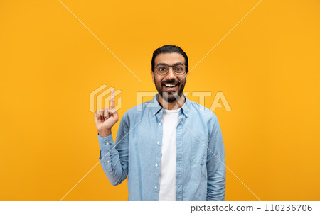 An excited man with a beard and glasses raises his index finger, sporting a bright smile 110236706