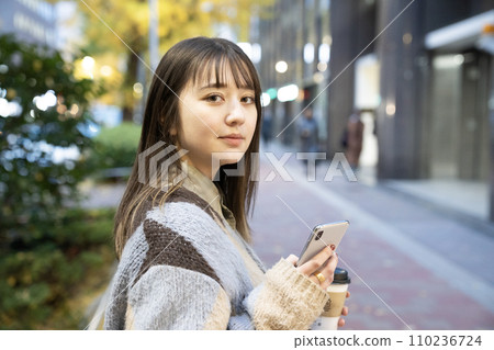 一位女士在戶外拿著智慧型手機並轉身 110236724