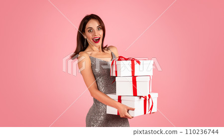 An overjoyed woman with wide eyes and a bright smile, dressed in a glittery silver dress 110236744