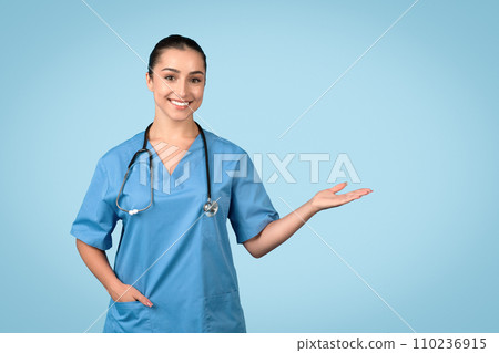 Confident female nurse presenting with hand in blue scrubs 110236915