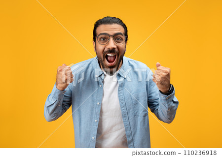 Euphoric man in blue denim shirt with clenched fists and mouth wide open 110236918