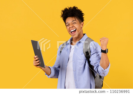 Exuberant black male student with tablet celebrating on yellow 110236991
