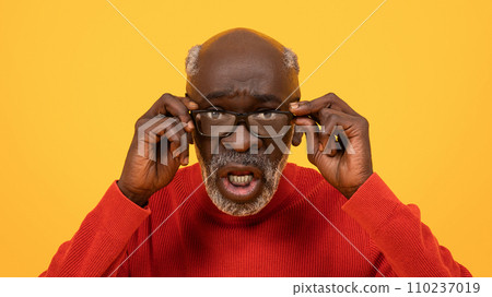 Surprised senior Black man adjusting his glasses with a puzzled expression 110237019