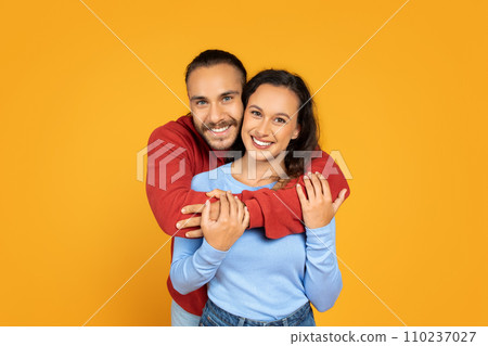 Attractive millennial couple hugging on orange background Attractive millennial couple hugging on orange background 110237027