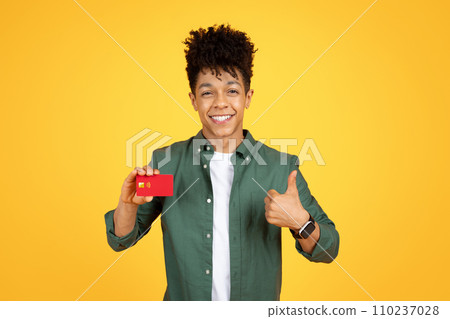 Cheerful african american guy showing credit card and thumb up Cheerful african american guy showing credit card and thumb up 110237028