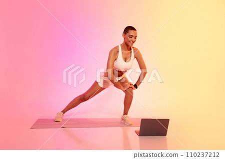 A fit woman with a buzz cut and sportswear stretches her leg muscles 110237212