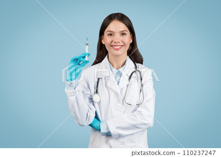 Young woman doctor with syringe on blue backdrop 110237247