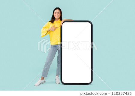 Cool stylish young brunette woman pointing at huge phone Cool stylish young brunette woman pointing at huge phone 110237425
