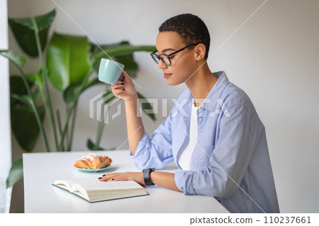 A contemplative young woman enjoys her morning coffee while reading A contemplative young woman enjoys her morning coffee while reading 110237661