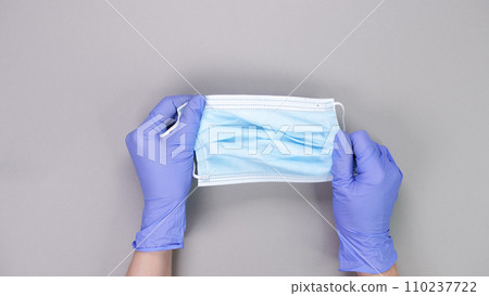 Hand in blue gloves of doctor or nurse holding protective blue face mask over grey background with copy space. New vaccine. Unknown vaccine. Medical gloves. Hand in blue gloves of doctor or nurse holding protective blue face mask over grey background with copy space. New vaccine. Unknown vaccine. Medical gloves. 110237722