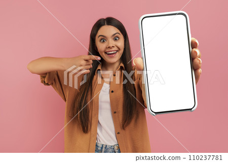 Cheerful Teen Girl Pointing At Blank Smartphone With White Screen In Hand 110237781