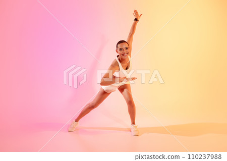 A joyful woman with a shaved head in a dynamic yoga pose, wearing a white sports outfit and sneakers 110237988