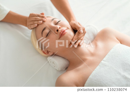 blonde woman enjoying facial massage lying on spa bed indoor blonde woman enjoying facial massage lying on spa bed indoor 110238074