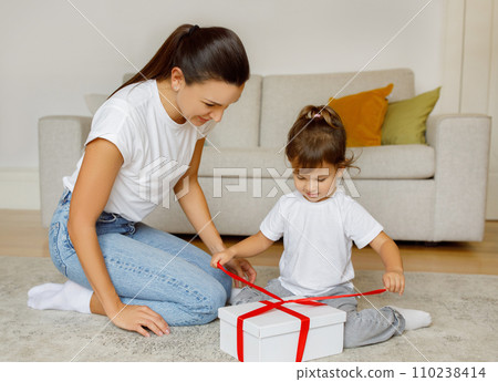Adorable Little Girl Unpacking Gift Box With Red Ribbon At Home Adorable Little Girl Unpacking Gift Box With Red Ribbon At Home 110238414