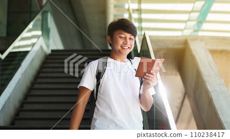 Happy young asian guy going down stairs, checking his tickets 110238417