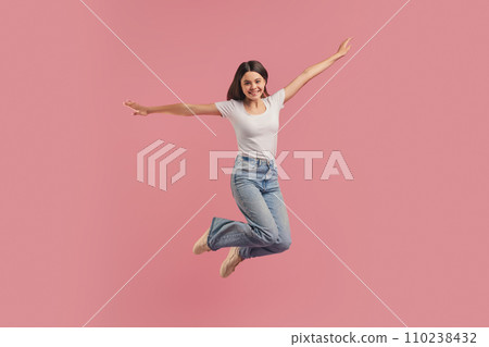 Joyful teenage girl mid-jumping with outstretched arms, expressing freedom and happiness Joyful teenage girl mid-jumping with outstretched arms, expressing freedom and happiness 110238432