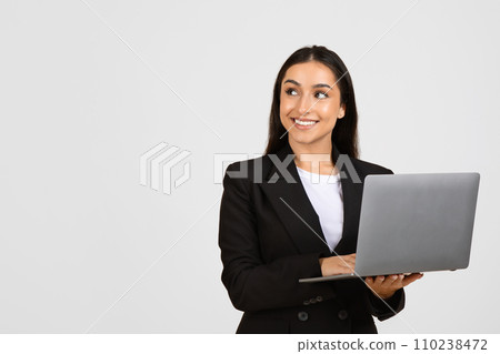 Smiling businesswoman holding laptop against grey background, free space 110238472