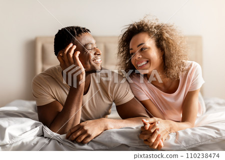 Smiling African American Young Spouses Lying Together In Comfortable Bed Smiling African American Young Spouses Lying Together In Comfortable Bed 110238474
