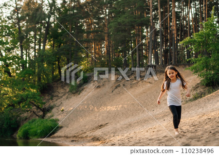 Happy little girl running on sandy beach close to river. Junior active athlete doing sports and having fun near water. 110238496