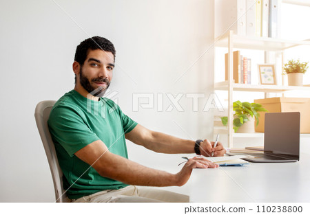 Smiling bearded man with glasses in a green shirt sitting at a desk Smiling bearded man with glasses in a green shirt sitting at a desk 110238800