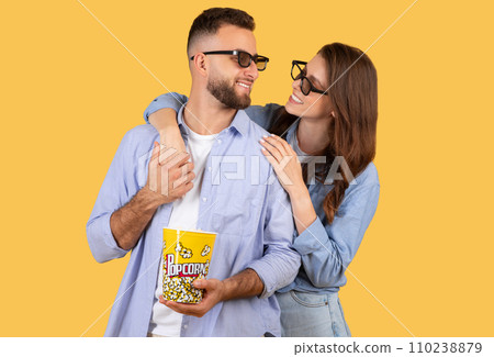 Excited young man and his girlfriend with 3D glasses and popcorn embracing, yellow studio background Excited young man and his girlfriend with 3D glasses and popcorn embracing, yellow studio background 110238879